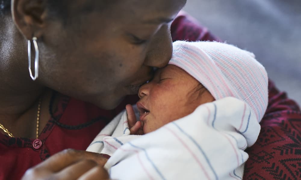 Caregiver pressing her lips to a sleeping baby's forehead.